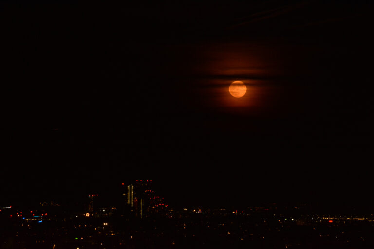 Strawberry moon rising over the Vienna skyline in a deep orange hue.