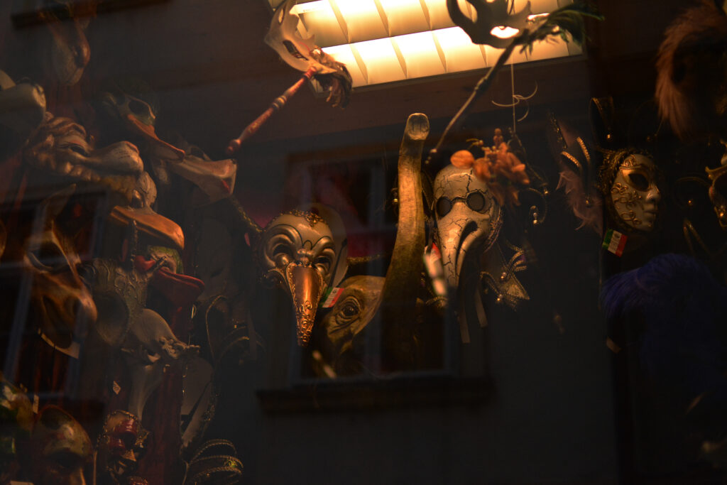 Urban photograph taken in Vienna’s Inner City showing a storefront with sculpted Venetian carnival masks displayed behind glass, framed by warm lighting and historic architectural elements.