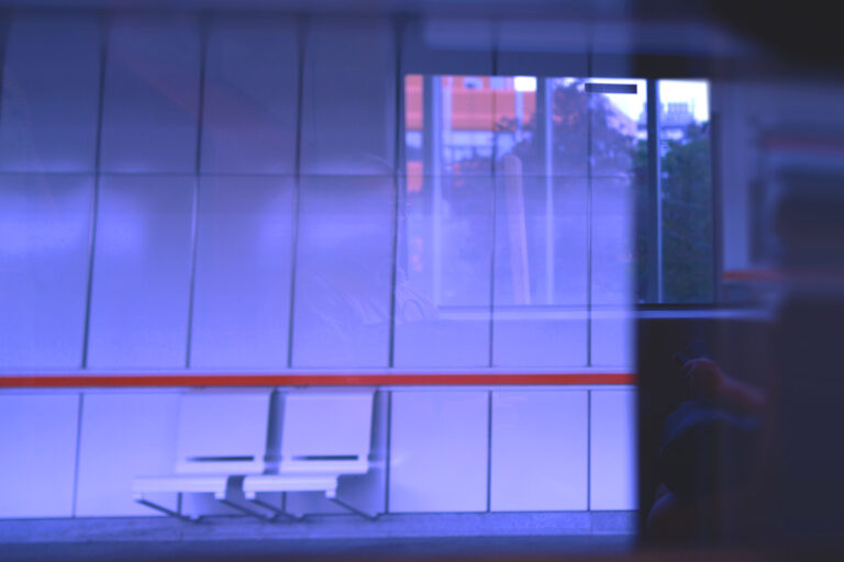 Urban photograph of a subway station on Vienna’s U3 line, featuring an arriving train, strong linear architecture, and contrasting warm and cool lighting.